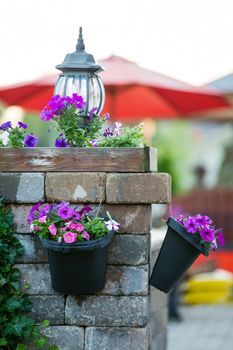 Detail of Stone Patio Pillar Decorated with Unlit Lamp and Purple Flowers in Hanging Pots - Recently Watered Flower Pots Hanging Off Stone Patio Pillar