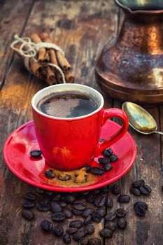 Red glass Cup with coffee on wooden background strewn with aromatic spices to drink