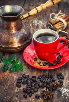 Red glass Cup with coffee on wooden background strewn with aromatic spices to drink