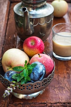 apples and plums in iron vase, teapot and cup of coffee