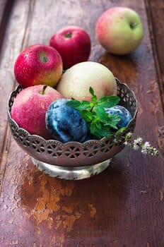 apples and plums in iron vase on strensham wooden background