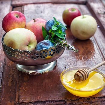 apples and plums in iron vase and saucer with fresh honey