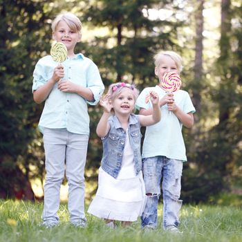 Group of happy children eating lollipops outdoors in summer park