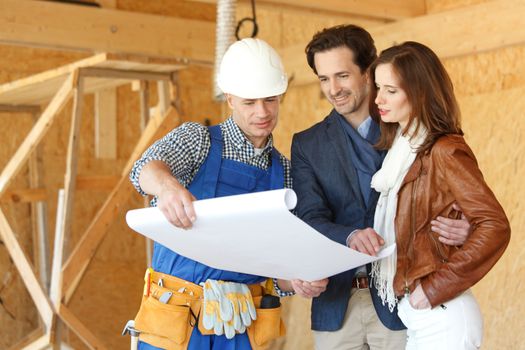 Worker shows house design plans to a young couple at construction site