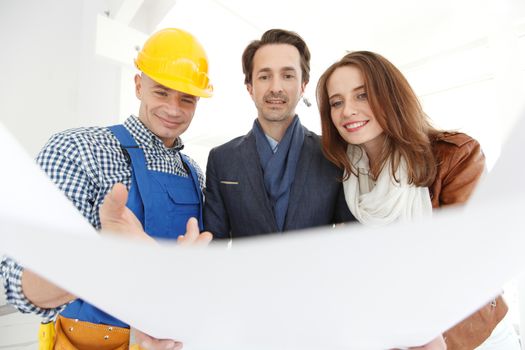 Worker shows house design plans to a young couple at construction site