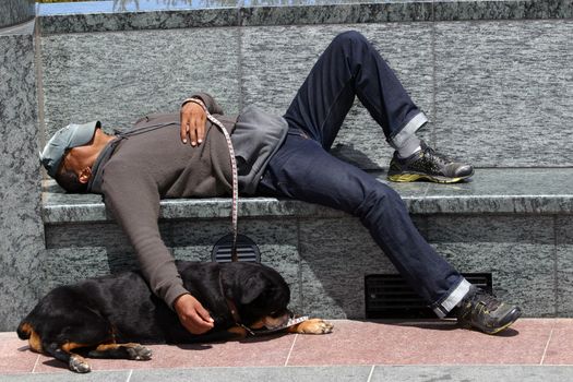 San Francisco, USA - July 24 2010: Homeless Man Sleeping on A Park Bench. The Rottweiler dog sleeps on the floor