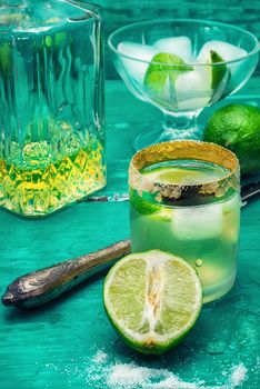 Glass with alcohol and fruits of lime and the bowl with ice  on wooden background