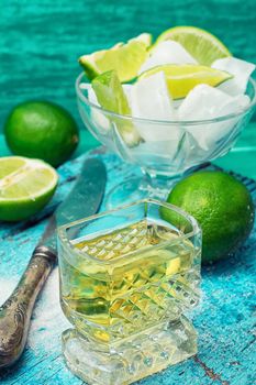 Glass with alcohol and fruits of lime and the bowl with ice  on wooden background