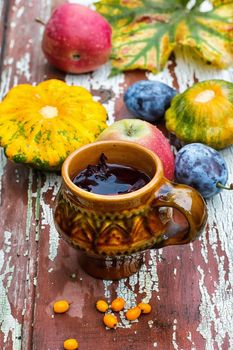 clay mug with herbal tea on  background of apples and plums in the autumn garden.Selective focus