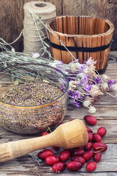 scattered medicinal Cornel berries and bowl of seeds of Heather on wooden table