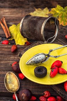 Dogrose berries and maple autumn leaves against the yellow saucer