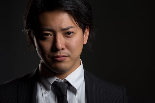 A low key portrait of a young Japanese man in a business suit with a hint of a smile on his face.