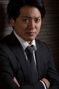 A low key portrait of a young Japanese man in a business suit with a serious expression on his face.