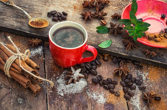 Red glass Cup with coffee on wooden background strewn with aromatic spices to drink