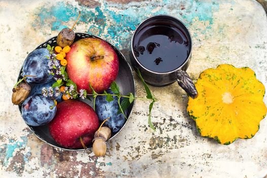 Mug with herbal medicinal tea on an autumn fruit,chestnuts and acorns on metal background.