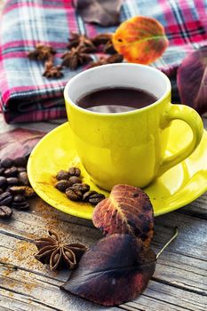 Yellow cup of black coffee on background with warm blanket strewn with autumn leaves