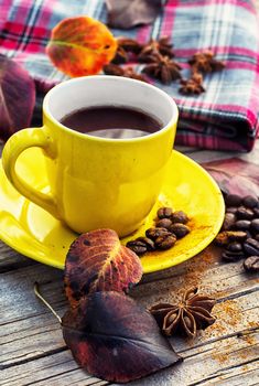 Yellow cup of black coffee on background with warm blanket strewn with autumn leaves