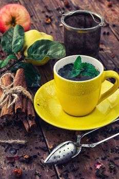 Cup of brewed herbal tea on wooden background strewn with tea leaves