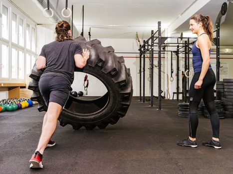 Photo of an attractive young woman and man working out with a tractor tire at a crossfit gym.