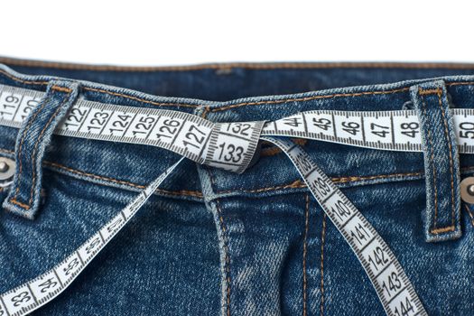 Waist check and excess weight control concept. Pair of blue jeans with measuring tape as belt having tied knot
