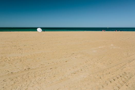 Mordialloc Beach in Melbourne. A large white umbrella near the waterline shelters its occupants.