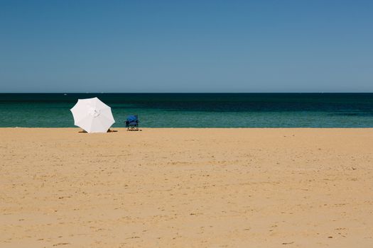 Mordialloc Beach in Melbourne. A large white umbrella near the waterline shelters its occupants.