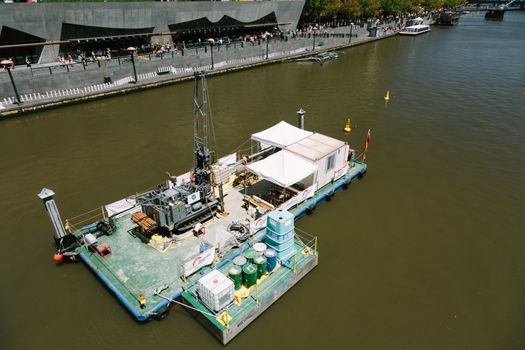 A dredging barch deepens the Yarra River in Melbourne. This photo was taken outside of the Arts Centre where large dominoes are being set up in the background.