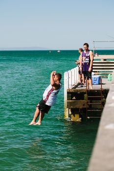 MELBOURNE/AUSTRALIA - FEBRUARY 6: Youths jump off a jetty into the water, while others fish in Mordialloc, a coastal suburb of Melbourne, Australia in February.