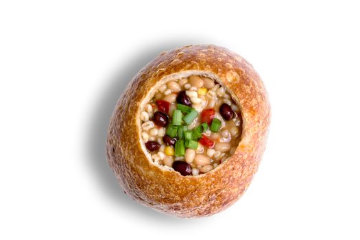 Top view of delicious bean and barley soup garnished with green onions inside bowl of bread