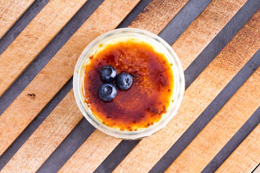 Above view of single little bowl full with custard dessert and toppings of blackberries on wooden cutting board