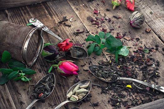 Stylish spoons with  variety of tea on vintage wooden board.