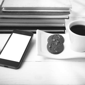 coffee cup with cookie,phone,stack of book and eyeglasses on white wood table black and white color