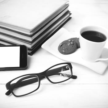 coffee cup with cookie,phone,stack of book and eyeglasses on white wood table black and white color