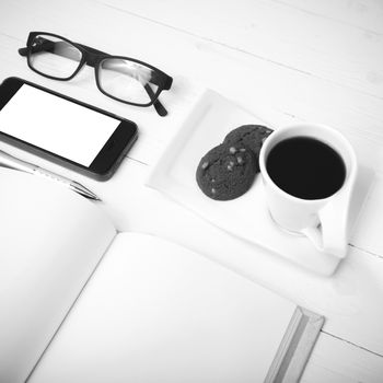 coffee cup with cookie,phone,notebook and eyeglasses on white wood table black and white color