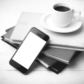 coffee cup with phone and stack of book on white wood table black and white color