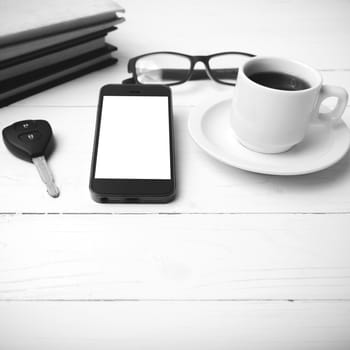 coffee cup with phone, car key,eyeglasses and stack of book on white wood table black and white color