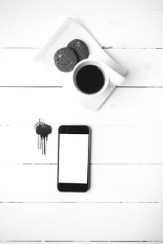 coffee cup with cookie,phone and key on white wood table black and white color