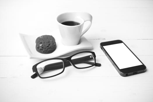 coffee cup with cookie,phone and eyeglasses on white wood table black and white color