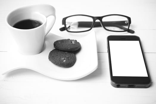 coffee cup with cookie,phone and eyeglasses on white wood table black and white color