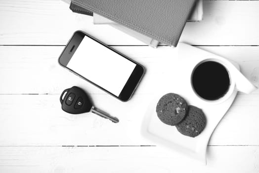 coffe cup with cookie,phone,car key and stack of book on white wood table black and white color