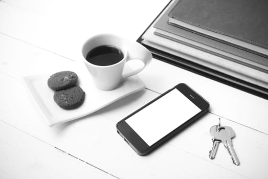 coffee cup with cookie,phone,stack of book and key on white wood table black and white color