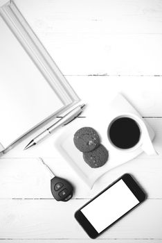 coffee cup with cookie,phone,open notebook and car key on white wood table black and white color