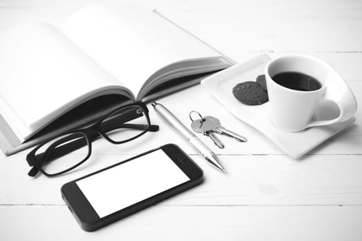 coffee cup with cookie,phone,open notebook and eyeglasses on white wood table black and white color