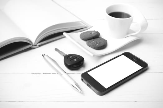coffee cup with cookie,phone,open notebook and car key on white wood table black and white color