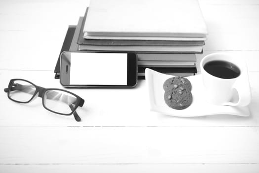 coffee cup with cookie,phone,stack of book and eyeglasses on white wood table black and white color