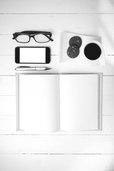 coffee cup with cookie,phone,notebook and eyeglasses on white wood table black and white color
