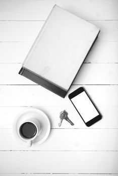 coffee cup with phone,key and stack of book on white wood table black and white color
