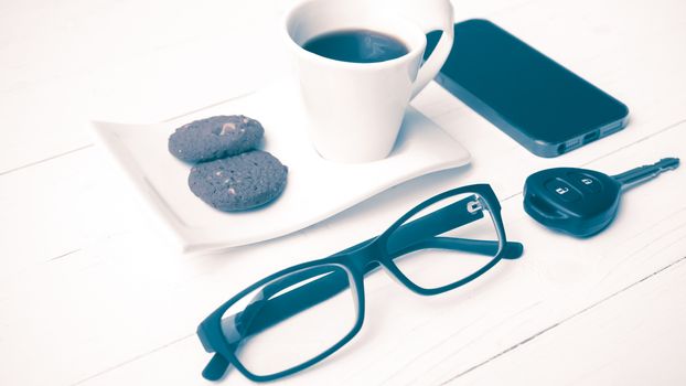 coffee cup with cookie,phone,eyeglasses and car key on white wood table vintage style