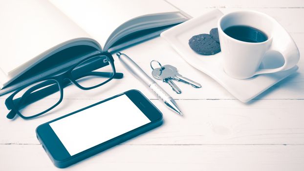 coffee cup with cookie,phone,open notebook and eyeglasses on white wood table vintage style