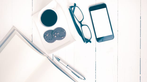 coffee cup with cookie,phone,notebook and eyeglasses on white wood table vintage style